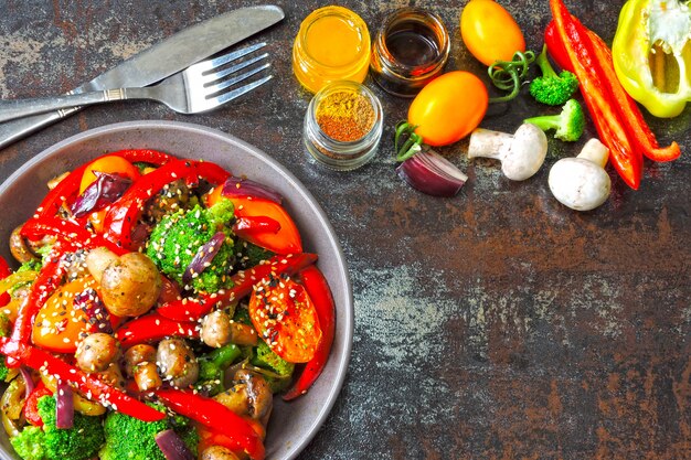 Warm salad with broccoli, mushrooms and red paprika. Vegan bowl with warm vegetables on a stylish shabby background. Healthy food. Fitness lunch with mushrooms and vegetables.