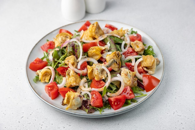 Warm salad with rapan snails tomatoes onions leafy vegetables and olive oil Traditional salad with seafood Closeup selective focus