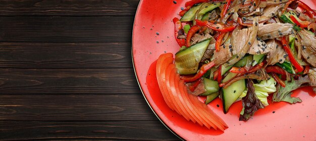 Warm salad with veal and vegetables on a red plate