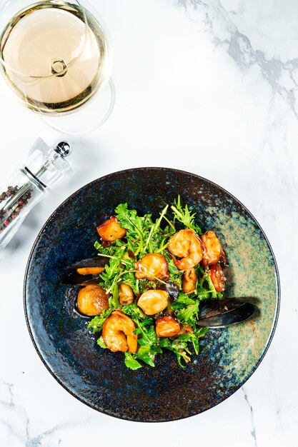 Warm seafood salad in a stylish black bowl on a marble table. Scallop salad. mussels, shrimps in sweet and sour sauce.