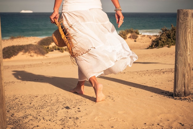 Warm summer holiday vacation travel in beach paradise resort concept with beautiful elegant woman viewed from back salking barefoot on the sand enjoying the sea water and outdoor