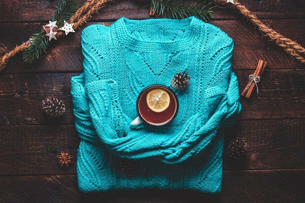 Warm sweater, pine cones, a mug of hot tea with lemon, cinnamon and aniseed stars. Winter clothes and drinks. Winter concept. 