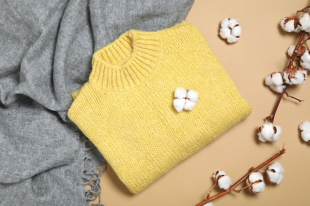 Warm sweater scarf and cotton flowers on beige background flat lay Autumn season