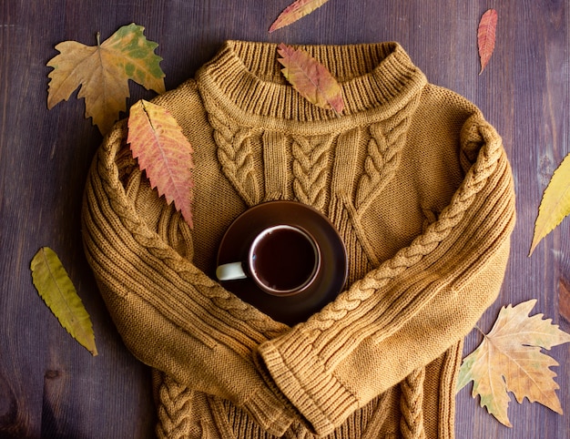 Foto le maniche calde del maglione abbracciano una tazza di caffè, la natura morta autunnale con caffè e foglie gialle