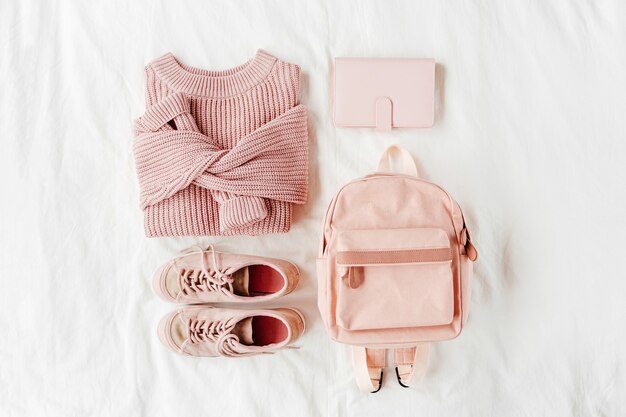 Warm sweater with backpack and sneakers in pale pink colored on bed. Women's stylish autumn or winter clothes. Cozy Winter look.  Flat lay, top view.