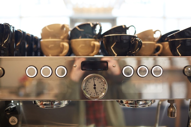 Foto immagine di sfondo dai toni caldi della macchina da caffè in acciaio nella caffetteria con tazze assortite, spazio copia