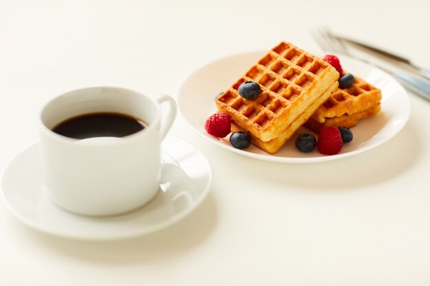 Warm-toned close up of sweet dessert waffles with berry topping next to cup of black coffee