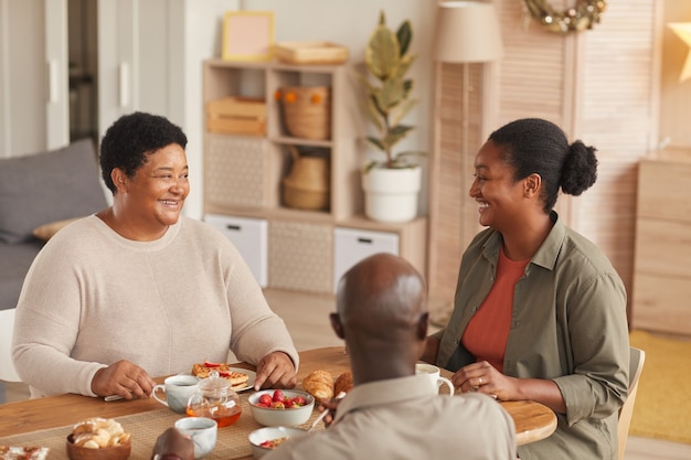 아늑한 인테리어에서 집에서 아침 식사를하면서 차와 간식을 즐기는 아프리카 계 미국인 가족의 따뜻한 톤의 초상화