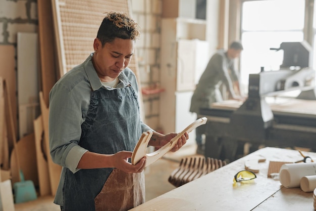 Warm toned portrait of female carpenter inspecting wooden furniture parts in sunlit workshop copy space