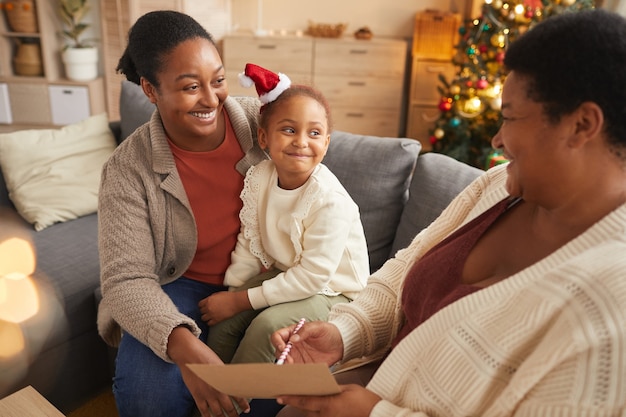 Warm-toned portrait of smiling African-American family writing letter to Santa with cute little girl while enjoying Christmas season at home