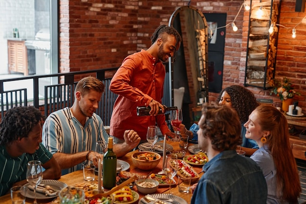 Warm toned shot of diverse group of friends enjoying dinner party in cozy cabin