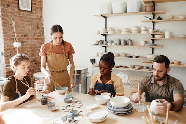 Warm toned shot of diverse group of people decorating ceramics in pottery workshop