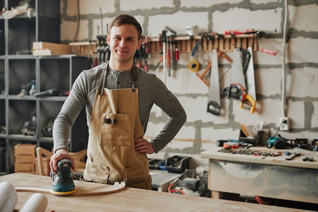 Warm toned shot of young carpenter smiling at camera while building furniture in workshop copy space