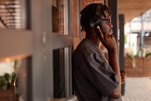 Warm toned side view portrait of young black man wearing headphones and listening to music while lea