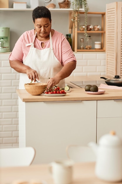 Warm toned vertical portrait of black grandma cooking in cozy home kitchen copy space