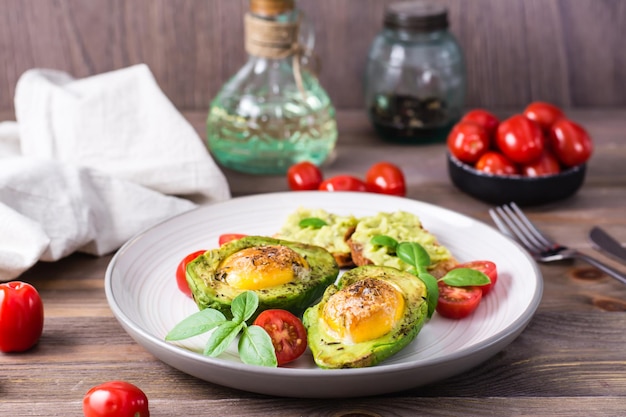 Warm voorgerecht gebakken avocado met ei, toast, cherrytomaatjes en basilicum op een bord op een houten tafel. gezond eten. flexitarisch dieet