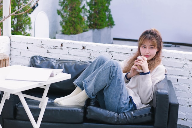 写真 暖かい冬の女の子がソファに座ってコーヒーを飲みながら読んでいる