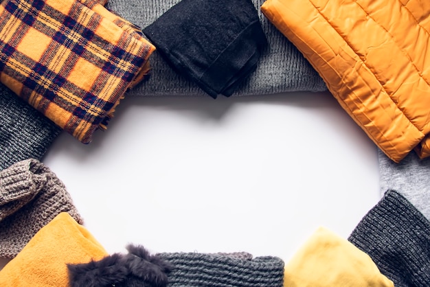 Warm winter wear on white background. Copy space. Yellow and grey trendy fashion colors. Knitted jumpers, jackets, mittens and plaids.