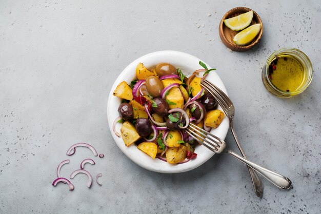 Warme aardappelsalade met olijven, peper, peterselie en rode ui op oude witte ceramische plaat op grijze concrete oppervlakte. Selectieve aandacht. Bovenaanzicht.