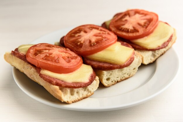 Warme broodjes met gesmolten kaasworst, salami en tomaten