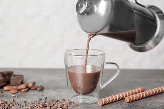 Warme cacaodrank gieten in glazen beker op keukentafel