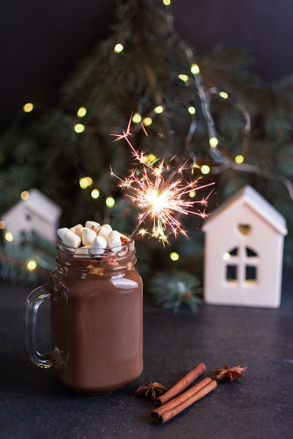 Warme chocolademelk in een glas met marshmallows op tafel met dennenboom kerstverlichting en decoraties