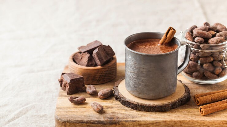 Warme chocolademelk in een metalen mok met een kaneelstokje op het tafellaken.
