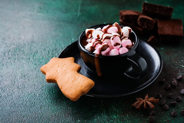 Warme chocolademelk met anijs en noten in zwarte keramische beker op oude donkergroene betonnen ondergrond. Selectieve aandacht.