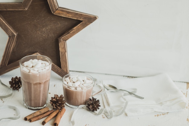 Warme chocolademelk met marshmallows. Decoraties met kaneel, dennenappel en witte servetten.