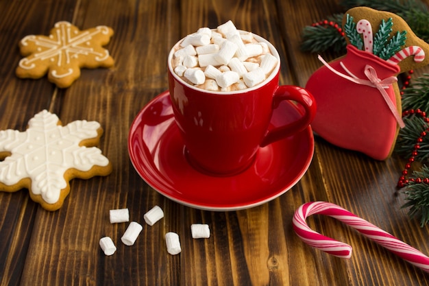 Warme chocolademelk met marshmallows in de rode kop en kerstkoekjes op de bruine houten achtergrond