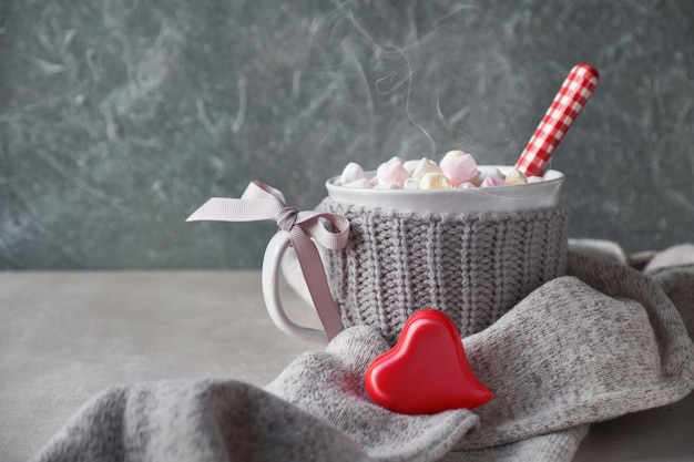 Warme chocolademelk met marshmallows, rood hart op de beker op de grijze steen