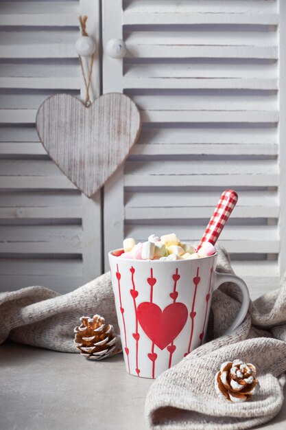 Warme chocolademelk met marshmallows, rood hart op de kop op de tafel met winterdecoraties