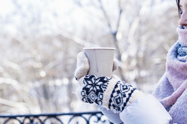 Warme drank in de handen van de vrouw met warme gebreide handschoenen op koude winterse besneeuwde dag.