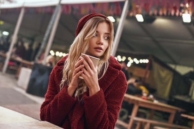 Warme drank in de herfst. Close-up van een vrouw die glühwein drinkt op de straatmarkt. Close-up foto van blonde vrouw die uitkijkt naar haar vriendje