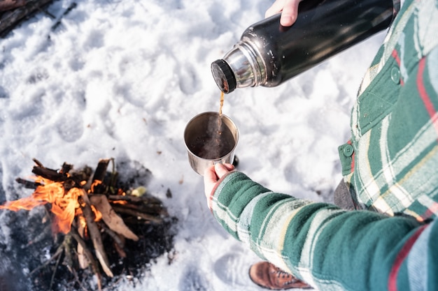 Warme drank uit een thermoskan gieten op een camping. Persoon die warm dichtbij een kampvuur, schot van het standpunt wordt