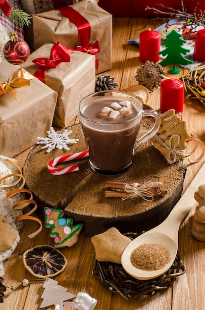 Foto warme kerst- en nieuwjaarsdrank van cacao met marshmallows op een tafel met geschenken, kerstkoekjes en kerstboomtakken. warme chocolademelk.