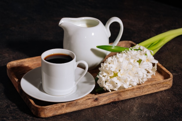 Warme koffie in witte kop melk en bloemen witte hyacint op houten dienblad