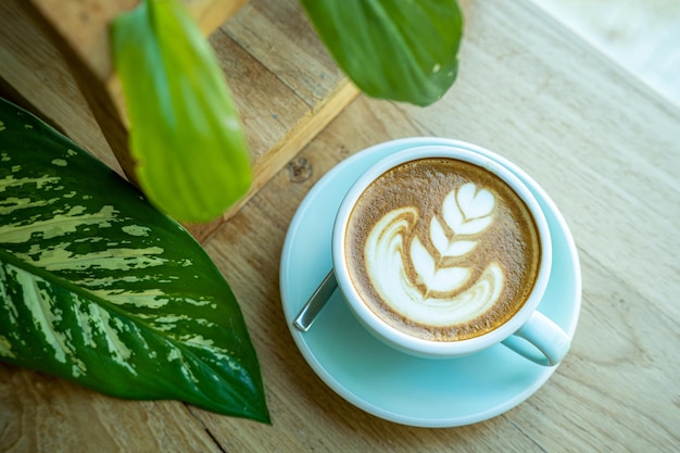 Warme koffie latte met latte art melkschuim in bekermok op houten bureau op bovenaanzicht als ontbijt in een coffeeshop in het caféduring zakelijk werkconcept