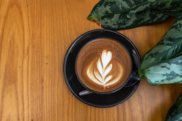 Warme koffie latte met latte art melkschuim in bekermok op houten bureau op bovenaanzicht als ontbijt in een coffeeshop in het caféduring zakelijk werkconcept