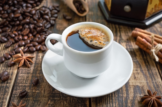 Warme koffie op een houten ondergrond met koffiebonen, handmatige koffiemolen, kaneelstokjes.