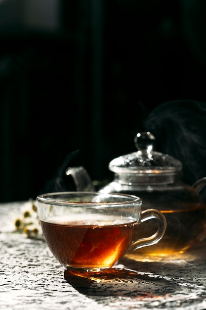 Warme kop thee met glazen theepot op donkere achtergrond