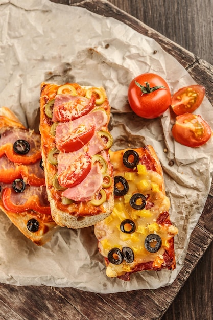 Warme pizza baguettes met olijven tomaten en ham op een houten tafel