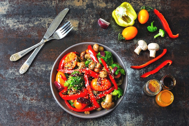 Warme salade met broccoli, champignons en rode paprika. Veganistische kom met warme groenten op een stijlvolle shabby achtergrond. Gezond eten. Fitness lunch met champignons en groenten.