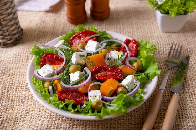 Warme salade met pompoen, fetakaas, zongedroogde tomaten, olijven, rucola en rode ui.