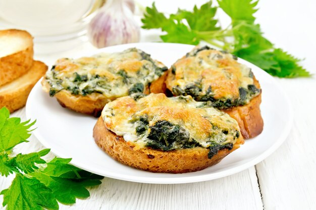 Warme sandwiches met brandnetels en kaas op sneetjes tarwebrood in een plaat, knoflook op een houten plankachtergrond