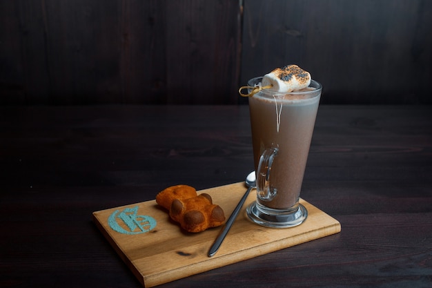 Warme zoete lekkere latte in een transparant glas met koekje versierd met luchtfoto marshmallow op een houten bord in een café