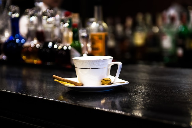 Foto warming cocktail alcolico in una tazza bianca, la barra con un bastoncino di cannella e un'arancia arancione