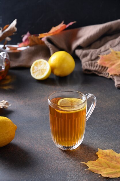 Warming black tea with lemon in cozy lifestyle with fall leaves and cozy scarf on brown space