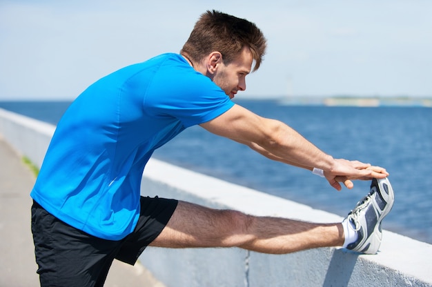 Warming up. Handsome young man doing stretching exercises while standing outdoors