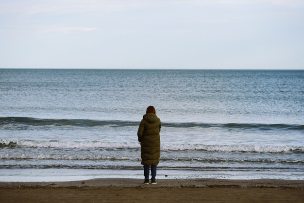 手を振る海の端に立っている温かい服装の女性